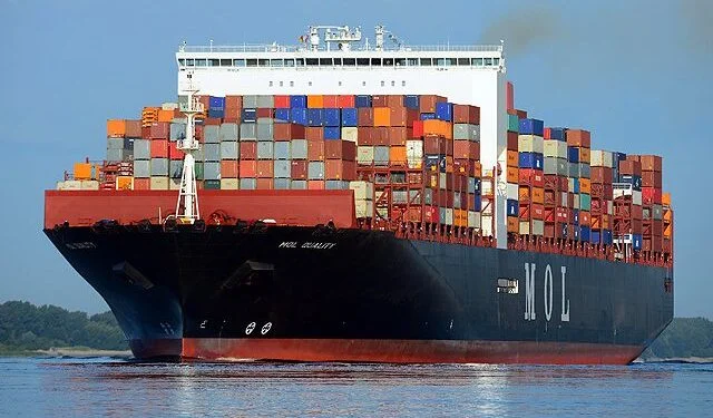 A loaded container vessel on the water, viewed from the bow.