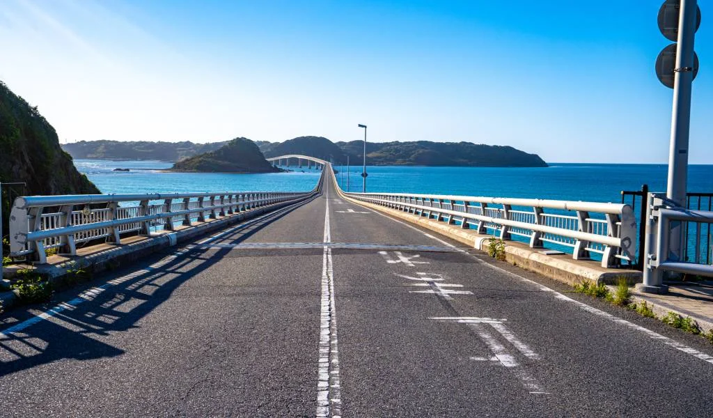 A coastal road crosses blue water towards green islands in Japan.